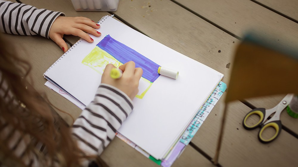 Ein Mädchen zeichnet die Flagge der Ukraine auf ein Blatt Papier