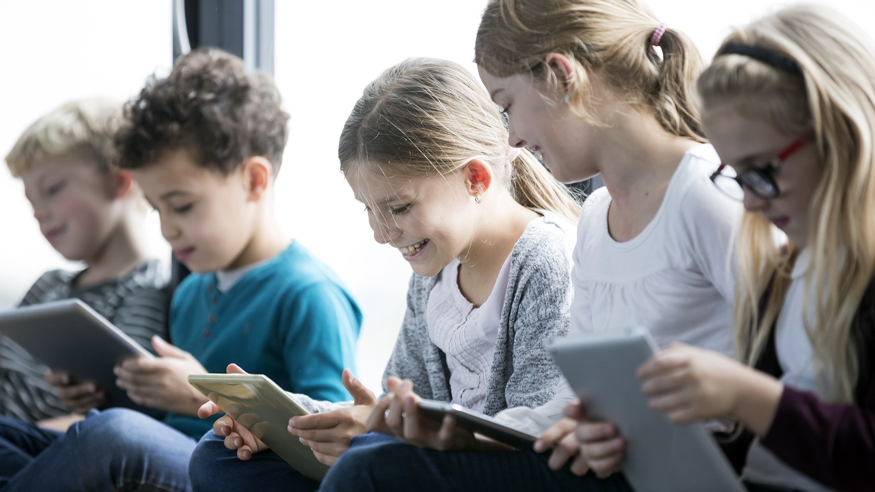 Cinq enfants travaillent à l'école avec des tablettes