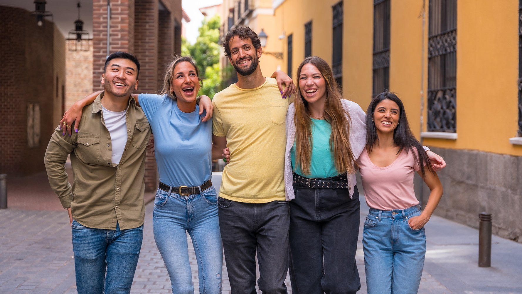 Cinq jeunes gens se tiennent dans une ruelle d'une ville du sud de l'Europe et s'étreignent.